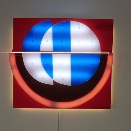 Entdecken Sie eine moderne Lichtplastik, die das Logo abstrakt interpretiert. Das Kunstwerk besteht aus einem Holz-Unterbau und mehreren Acrylglas-Scheiben, die mit weißen LEDs hinterleuchtet werden. Ideal für zeitgenössische Innenräume, Galerien und lichtbasierte Kunstinstallationen.